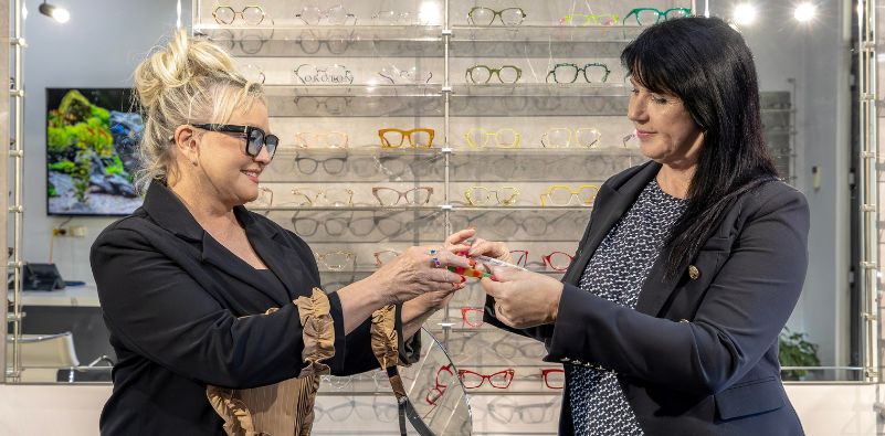 Optical dispenser presenting fitted prescription glasses during an eyewear consultation.